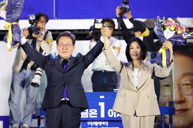 제21대 대통령 당선이 확실시되는 더불어민주당 이재명 대선 후보와 부인 김혜경 여사가 4일 서울 여의도 국회 인근에서 당 주최로 열린 국민개표방송 행사에 참석해 꽃다발을 받고서 시민들을 향해 두 팔을 들어올려 인사하고 있다. /연합