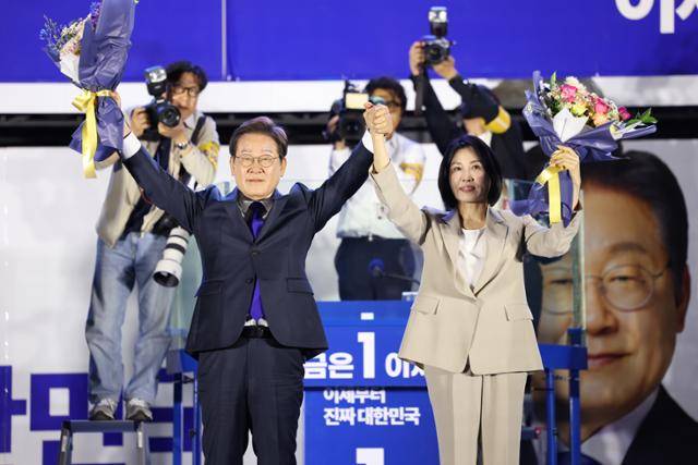제21대 대통령 당선이 확실시되는 더불어민주당 이재명 대선 후보와 부인 김혜경 여사가 4일 서울 여의도 국회 인근에서 당 주최로 열린 국민개표방송 행사에 참석해 박찬대 상임총괄선대위원장과 정은경 총괄선대위원장단으로부터 꽃다발을 받은 뒤 시민들을 향해 두 팔을 들어 인사하고 있다. 연합뉴스