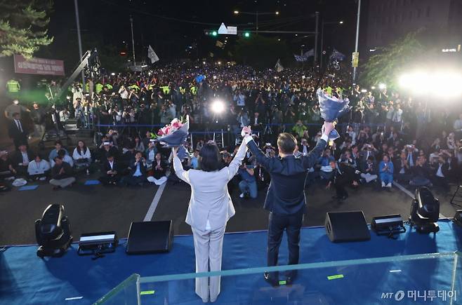 [서울=뉴시스] 조성우 기자 = 이재명 대통령과 김혜경 여사가 4일 오전 서울 여의도 국회 앞에서 열린 국민 개표방송 행사에서 꽃다발을 받은 뒤 시민들을 향해 인사하고 있다. (공동취재) 2025.06.04.