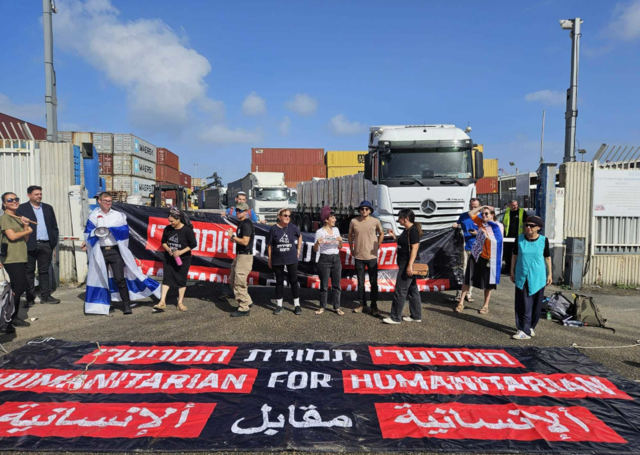 27일 오전 이스라엘 서부 항구도시 아시도드에서 보수성향 시민단체 ‘오더 9’ 회원들이 ‘인도주의를 위한 인도주의’라고 영어, 히브리어, 아랍어 등으로 쓰인 플래카드를 들고 구호품을 싣고 가자지구로 향하는 트럭 앞을 막아서고 있다. X 캡처.