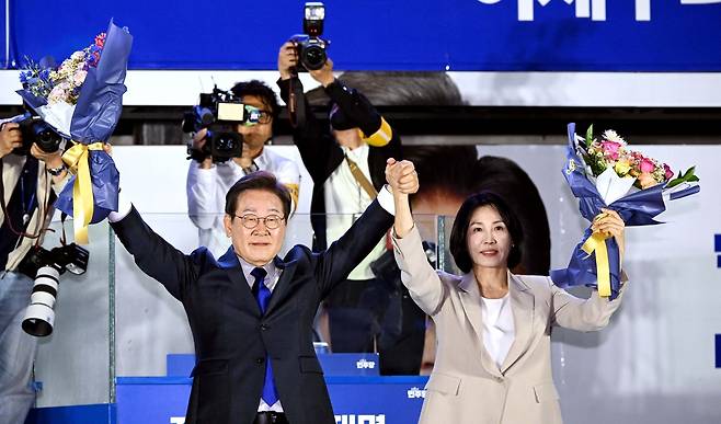 제21대 대통령 당선이 확실시되는 더불어민주당 이재명 대선 후보와 부인 김혜경 여사가 4일 서울 여의도 국회 인근에서 당 주최로 열린 국민개표방송 행사에 참석해 꽃다발을 받고서 시민들을 향해 두 팔을 들어 인사하고 있다. 2025.6.4 [연합]