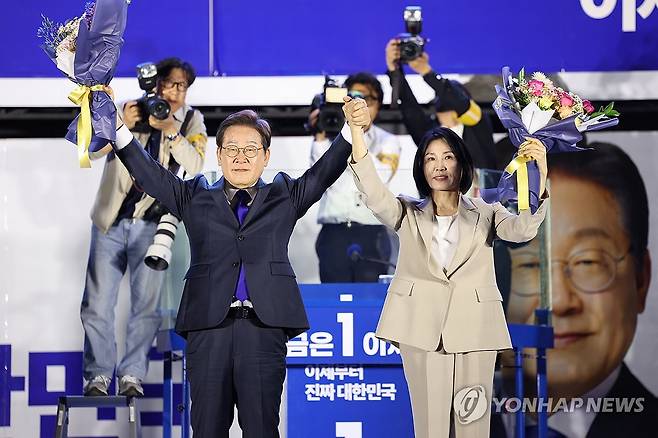축하 꽃다발 받는 이재명 후보와 김혜경 여사 (서울=연합뉴스) 김주성 기자 = 제21대 대통령 당선이 확실시되는 더불어민주당 이재명 대선 후보와 부인 김혜경 여사가 4일 서울 여의도 국회 인근에서 당 주최로 열린 국민개표방송 행사에 참석해 박찬대 상임총괄선대위원장과 정은경 총괄선대위원장단으로부터 꽃다발을 받고 시민들을 향해 두 팔을 들어 인사하고 있다. 2025.6.4 [공동취재] utzza@yna.co.kr