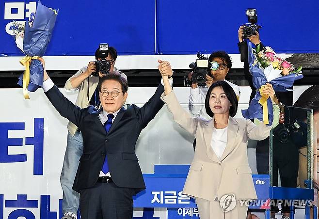 시민들 향해 인사하는 이재명 후보 내외 (서울=연합뉴스) 김주성 기자 = 제21대 대통령 당선이 확실시되는 더불어민주당 이재명 대선 후보와 부인 김혜경 여사가 4일 서울 여의도 국회 인근에서 당 주최로 열린 국민개표방송 행사에 참석해 꽃다발을 받고서 시민들을 향해 두 팔을 들어 인사하고 있다. 2025.6.4 [공동취재] utzza@yna.co.kr