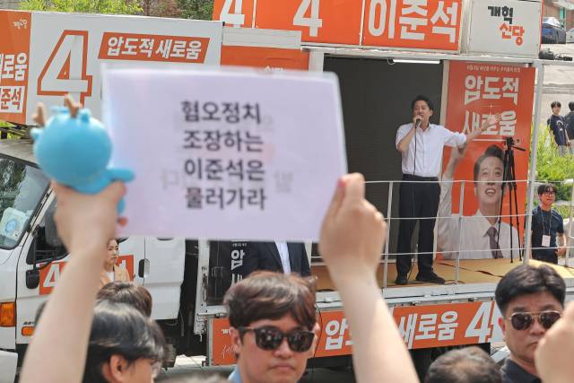 개혁신당 이준석 대선 후보가 지난달 30일 서울 동작구 중앙대학교에서 유세 중인 가운데 일부 학생들이 규탄 팻말을 들고 있다. 연합뉴스
