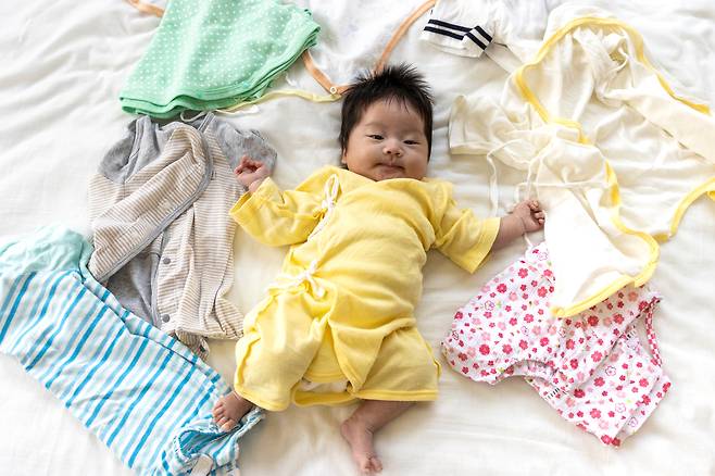 A baby is surrounded by lots of clothes. (123rf)