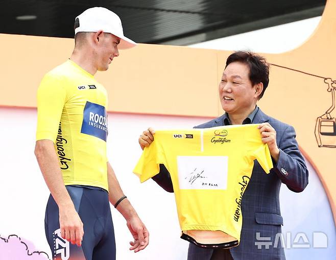 [창원=뉴시스]박완수 경남도지사가 8일 도청광장에서 열린 경남도 주최 '투르 드 경남 2025' 종합시상식에서 개인종합 우승을 차지한 루자이 인슈어런스 소속 호주 출신 호킨스 딜런 선수에게 '옐로우 저지(Yellow Jersey)' 티셔츠를 수여하고 있다.(사진=경남도 제공) 2025.06.08. photo@newsis.com