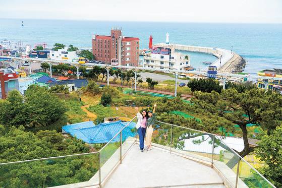 A Taiwanese mother and daughter pair take a photo with the Sky Capsule and Cheongsapo twin lighthouses in the background in Busan. [BAEK JONG-HYUN]