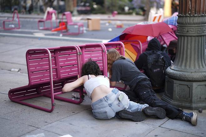 도널드 트럼프 행정부의 불법이민 단속에 항의하는 시위대가 8일(현지시간) 로스앤젤레스 도심 구치소 인근 의자 뒤에 숨어 시위를 벌이고 있다.