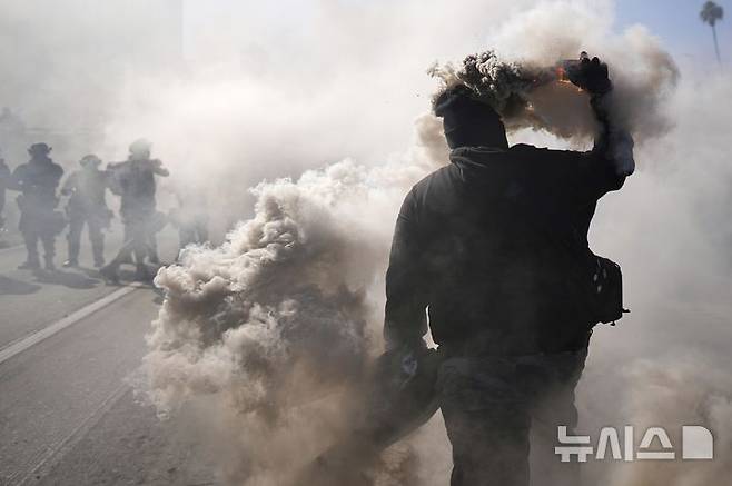 [로스앤젤레스=AP/뉴시스] 8일(현지 시간) 미 캘리포니아주 로스앤젤레스 도심 메트로폴리탄 구치소 인근 101번 고속도로에서 이민세관단속국(ICE)의 불법 이민자 단속 및 체포에 항의하는 시위 참가자가 경찰을 향해 연막탄을 던지고 있다. 2025.06.09.
