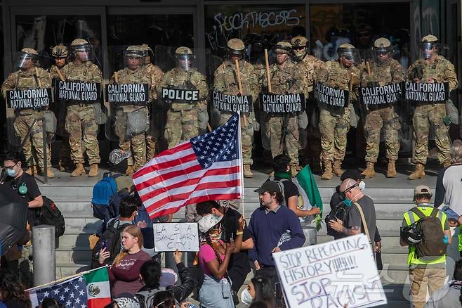 2025년 6월 9일 로스앤젤레스에서 연방 이민 작전에 반대하는 시위대가 연방 건물 밖에서 경비를 서고 있는 캘리포니아 주방위군 대원들을 향해 피켓과 깃발을 들고 있다. ⓒ AFP=뉴스1 ⓒ News1 신기림 기자