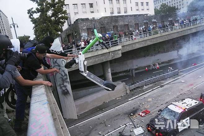 [로스앤젤레스=AP/뉴시스] 8일(현지 시간) 미 캘리포니아주 로스앤젤레스 도심 메트로폴리탄 구치소 인근 101번 고속도로 육교에서 이민세관단속국(ICE)의 불법 이민자 단속에 항의하는 시위대가 경찰차를 향해 스쿠터를 던지고 있다. 2025.06.09.