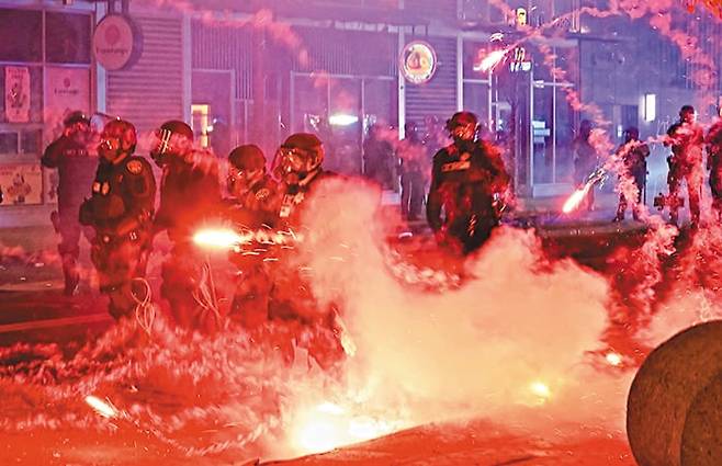 9일 오후 미국 로스앤젤레스(LA)의 일본인 타운 ‘리틀도쿄’ 거리에서 중무장한 경찰이 시위대가 발사한 폭죽 불꽃을 뚫고 진압 작전을 벌이고 있다. 불법 이주자 추방 반대 시위 나흘째인 이날, 본지가 현장에서 만난 시민들은 “트럼프는 오늘날 미국을 일궈낸 이민자들을 악마로 만들고 있다”고 했다. /AFP 연합뉴스