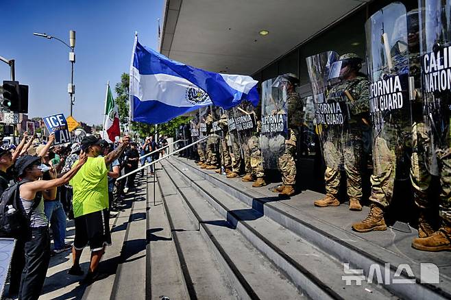 [로스앤젤레스=AP/뉴시스] 도널드 트럼프 미국 대통령이 로스앤젤레스(LA) 이민 단속 반발 시위를 빌미로 민간 영역에 대한 군 투입을 일상화하고 있다는 우려가 나오고 있다. 사진은 9일(현지 시간) LA 도심 연방 청사 앞에서 불법 이민자 단속에 반대하는 한 시위 참가자가 엘살바도르 국기를 흔들며 캘리포니아주 방위군과 대치하는 모습. 2025.06.10.