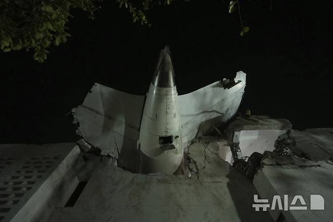 [아마다바드=AP/뉴시스] 12일(현지 시간) 인도 구자라트주 아마다바드에서 발생한 여객기 추락 사고 현장에 비행기 꼬리 부분이 건물에 박혀 있다. 이날 오후 아마다바드 공항에서 이륙한 영국행 에어인디아 AI171편 여객기가 추락해 탑승자 242명 가운데 1명을 제외한 전원이 숨졌으며, 추락 현장의 학생 등 약 50명도 사망한 것으로 전해졌다. 2025.06.13.