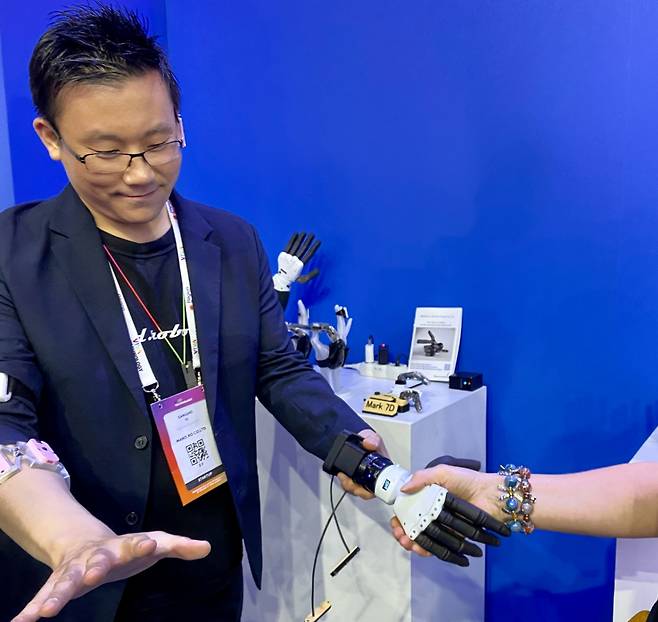 이상호 만드로 대표 오른팔에 낀 센서(분홍색)가 근육 신경을 감지, 왼손에 들고 있는 의수(로봇손)를 움직여 방문객과 악수하고 있다. 실제 손을 잃은 장애인이 의수를 착용하면 같은 원리로 의수를 조작할 수 있다./사진=김성휘 기자