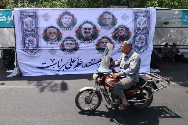 13일 이스라엘의 이란 공습으로 이란의 주요 군사 지도자들 및 핵과학자들이 사망한 가운데 수도 테헤란의 한 담벼락에 걸린 사망자 추모 걸개그림 앞을 한 남성이 오토바이를 타고 지나가고 있다. AFP 연합뉴스