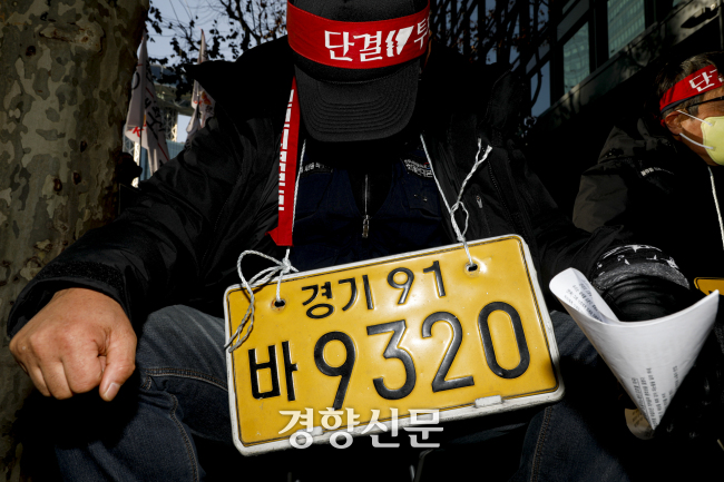 화물연대 파업 14일째인 2022년 12월7일 서울 종로구 SK에너지 앞에서 열린 화물연대 결의대회에 참석한 한 조합원이 목에 자신의 차량 번호판을 매단 채 자리에 앉아 있다. 문재원 기자
