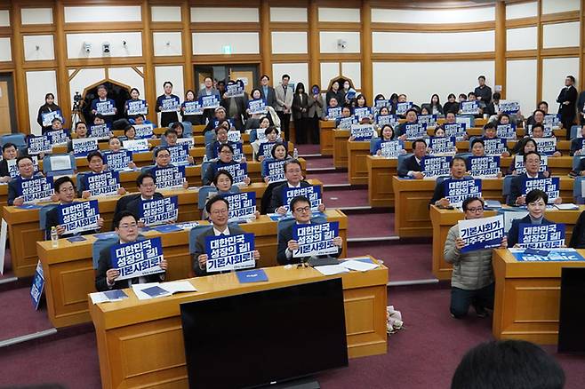 지난 3월11일 서울 여의도 국회 의원회관에서 열린 더불어민주당 서울 기본사회위원회 발대식에서 참석자들이 피켓을 들고 구호를 외치고 있다.  〈민주당 박주민 의원실 제공〉