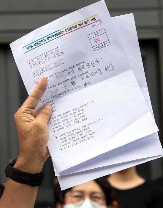 2021년 서울대학교 행정관 앞에서 열린 기자회견에서 민주노총 조합원이 청소 노동자들이 본 시험지 일부를 들어 보이고 있다. 사진=연합뉴스