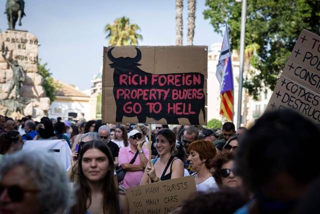 15일 스페인 마요르카섬에서 과잉 관광에 반대하는 시위가 열렸다. 한 시위 참여자가 “부유한 외국 부동산 구매자는 지옥에 간다”라고 쓰인 피켓을 들고 있다. AFP 연합뉴스