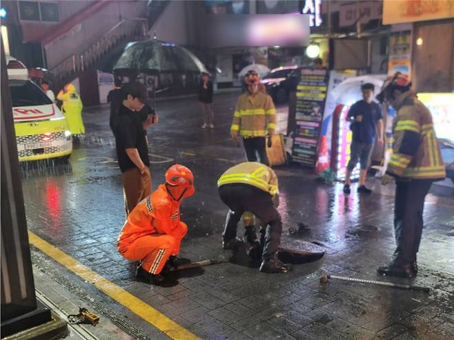 14일 부산 연제구의 한 도로에서 호우로 인해 맨홀 뚜껑이 열려 안전조치가 이뤄졌다. 부산소방재난본부 제공