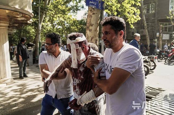 [테헤란=AP/뉴시스] 15일(현지 시간) 이란 테헤란에서 이스라엘의 공습으로 발생한 폭발로 부상한 남성이 부축을 받으며 대피하고 있다. 2025.06.17.