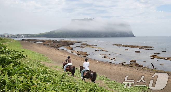 19일 오전 제주 서귀포시 성산읍 광치기해변에서 관광객들이 해무 낀 성산일출봉을 배경으로 승마체험을 하고 있다. 2025.6.19/뉴스1 ⓒ News1 오현지 기자