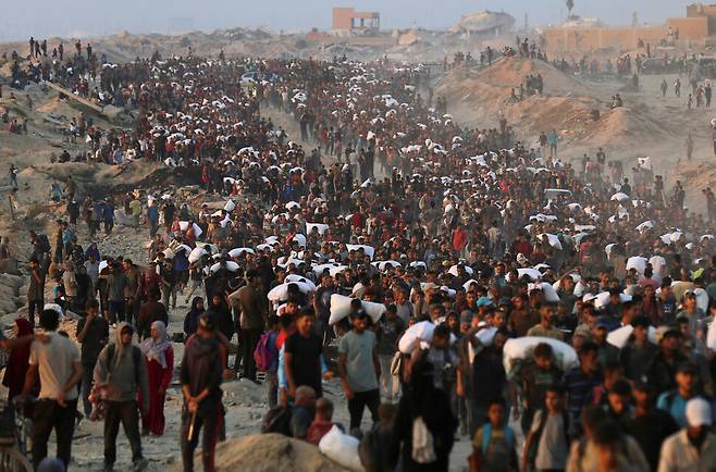 2025년 6월17일 팔레스타인 땅 가자지구 북부 베이트라히야에서 주민들이 밀가루 등 구호품을 배급받아 옮기고 있다. REUTERS 연합뉴스