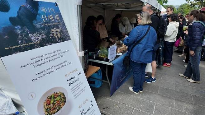 지난달 16일 프랑스 파리 시테대학교에서 열린 K플러스 페스티벌에서 관람객들이 해녀가 채취한 해산물로 만든 '해녀의 신세계' 뿔소라비빔밥과 제주 특산 메뉴 등을 구매하기 위해 줄을 서고 있다. 신세계백화점 제공