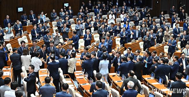이재명 대통령이 추경안 시정연설을 위해 본회의장에 들어서자 더불어민주당 의원들이 자리에서 일어나 환대하고 있다.
