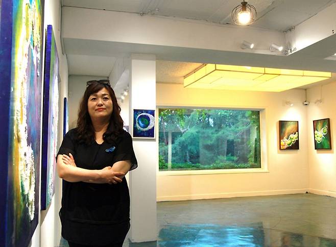 전시 공간에서 자신의 작품 앞에 선 서양화가 주명선 작가. 그는 암염의 자연 변화를 통해 생명력과 회복의 메시지를 전하는 ‘암염화’라는 독창적 회화 장르를 개척해왔다. 이번 전시는 남양주 산들소리 나눔 갤러리 블루 개관 기념 초대전이다. 주명선 작가 제공