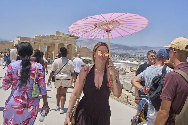 26일(현지시각) 그리스에 올여름 첫 폭염이 찾아와 기온이 40도를 넘길 것으로 예상되는 가운데, 양산을 든 관광객이 아크로폴리스 언덕에 있는 고대 프로필라이아 신전 앞을 걷고 있다. 아테네/AP 연합뉴스