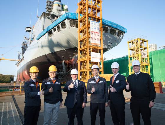 U.S. Secretary of the Navy John Phelan, third from left, and Hanwha Group Vice Chairman Kim Dong-kwan, fourth from left, along with other officials, pose for a commemorative photo in front of the USNS Yukon, which is undergoing maintenance at Hanwha Ocean’s Geoje shipyard on April 30. [HANWHA OCEAN]