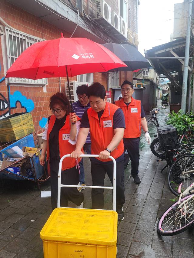 봉사단이 빗 속에 우산을 쓰고 쪽방촌 골목길을 걸어가는 모습.