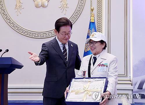 이재명 대통령이 27일 청와대 영빈관에서 열린 '호국 보훈의 달, 대통령의 초대' 행사에서 6.25 참전 용사인 이춘자씨에게 광목 이불을 선물하는 모습. [사진 제공] 연합뉴스