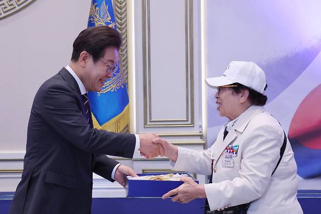 이재명 대통령이 27일 청와대 영빈관에서 열린 '호국 보훈의 달, 대통령의 초대' 행사에서 6·25전쟁에 참전해 유격대원으로 활약했던 여성 참전유공자 이춘자 참전용사에게 광목이불을 선물하고 있다. 연합뉴스
