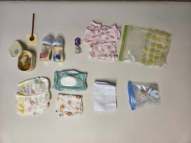 (왼쪽 위에서부터 시계방향으로)이유식과 치즈와 아기수저, 분유 가루만 담아놓은 젖병, 쪽쪽이, 여벌 옷, 이유식 담는 큰 지퍼백, 쪽쪽이 담는 작은 지퍼백, 현재는 카카오톡으로 대체한 이유식 및 대소변 기록지, 물티슈와 거즈 수건, 기저귀. /사진=최우영 기자