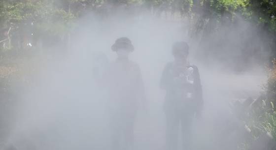 As cooling fog sprays from a mist system along a walking path in Jung District, Daegu, on June 30, people use handheld fans and personal fans to keep cool. [YONHAP]