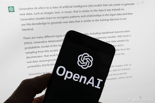 ChatGPT의 출력이 표시되는 컴퓨터 화면 앞에 있는 휴대폰에 OpenAI 로고가 보인다.  /AP=뉴시스