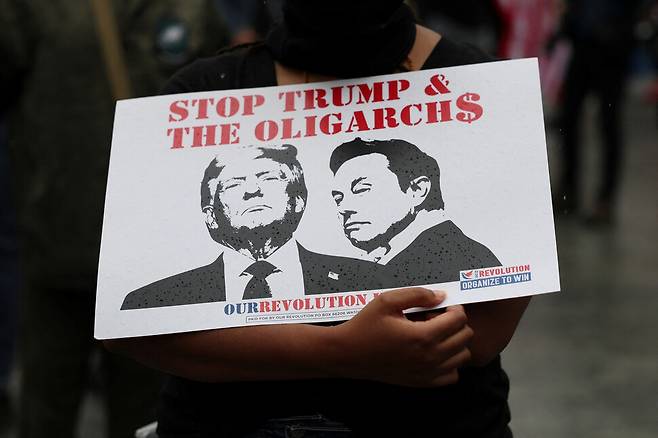 2025년 6월14일 미국 필라델피아에서 열린 반정부 시위에서 한 참석자가 도널드 트럼프 대통령과 일론 머스크를 묘사한 표지물을 들고 있다. 머스크는 트럼프의 감세안에 대해 ‘역겹고 추악한 괴물’이라며 공개 비판했다. REUTERS