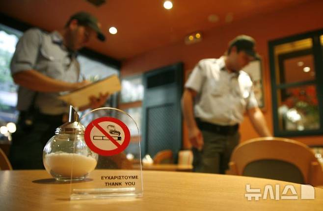 [아테네(그리스)=AP/뉴시스]2010년 9월1일 그리스 아테네 시내의 한 커피숍에서 경찰이 금연 표지판을 살펴보고 있다. 그리스 의회가 흡연과 음주로부터 어린이들을 보호하기 위해 술과 담배를 판매할 때 엄격한 연령 확인 규정을 제정하고, 특정 공공장소에서의 흡연을 금지하고 광고도 제한하는 법안을 통과시켰다고 유로뉴스가 4일 보도했다. 2025.07.06.