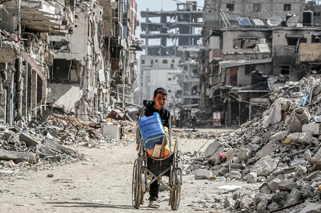 지난해 7월 가자지구 남부 최대 도시 칸유니스에서 한 팔레스타인 아이가 물통이 든 수레를 끌고 폐허가 된 거리를 지나고 있다. AFP연합뉴스