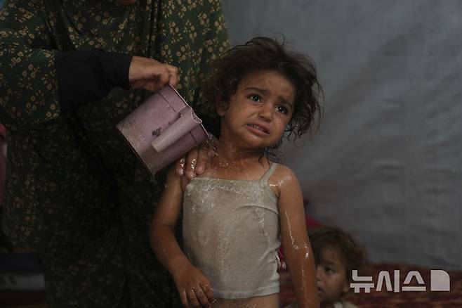 [칸유니스=AP/뉴시스] 지난 1일(현지 시간) 가자지구 남부 칸유니스 난민촌 텐트 안에서 한 팔레스타인 여성이 두 살 된 딸에게 소량의 물을 적셔주며 더위를 식혀주고 있다. 이스라엘 카츠 이스라엘 국방장관은 7일 가지 주민을 남부 라파에 수용할 것이라고 발표했다. 2025.07.08.