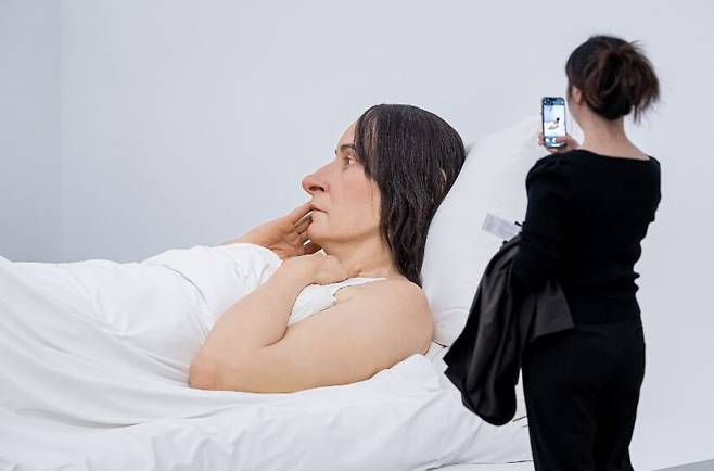 한 관람객이 전시장에서 론 뮤익 작품 '침대에서'를 휴대폰으로 찍고 있다. 침대에 누운 여성을 재현한 가로 6m 대형 조각이다. /국립현대미술관