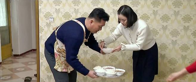 북한 드라마 '백학벌의 새봄' 중 한 장면 (서울=연합뉴스) 북한 드라마 '백학벌의 새봄' 속 남성이 꽃무늬 앞치마를 입고 아내와 딸에게 밥을 차려주고 있다. 2025.7.10 [조선중앙TV 캡처]