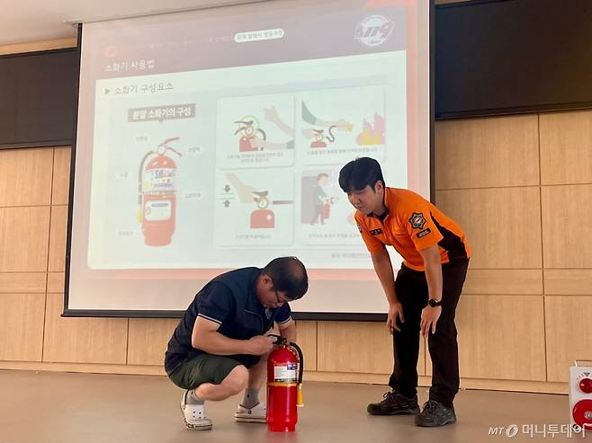 10일 오후 서울 관악경찰서에서 한 자율방범대원이 실습용 소화기 안전핀을 뽑는 모습을 소방관이 지켜보고 있다./사진=이현수 기자.