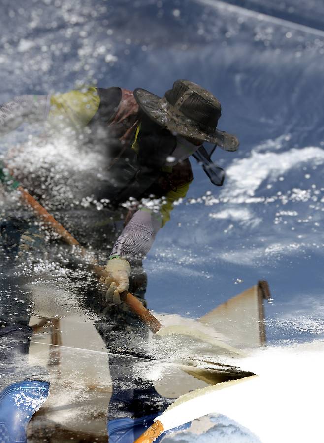 염부 전동길 씨가 결정지에서 소금삽을 들고 소금을 긁어모으고 있다. 사진은 결정지에 반영된 전동길씨 모습이다.