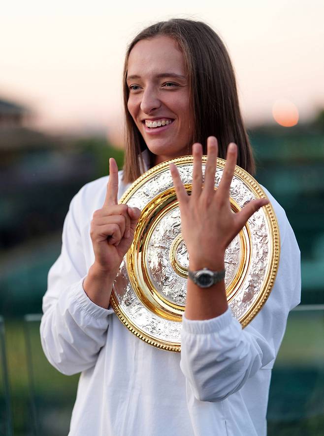 폴란드의 이가 시비옹테크가 2025년 7월 12일(토) 영국 런던에서 열린 윔블던 테니스 선수권 대회 여자 단식 결승전에서 미국의 아만다 아니시모바를 꺾고 우승한 뒤, 자신의 커리어 그랜드슬램 여섯 번째 우승을 의미하는 손가락 제스처 '6'을 하며 우승자에게 수여되는 비너스 로즈워터 디시의 복제품과 함께 포즈를 취하고 있다.