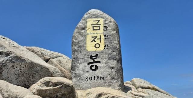 지난 11일 금정산 고당봉의 표지석에 누군가가 ‘금정’이란 글이 적힌 종이가 붙어있다. 금정구측은 현재 금정 글자가 적인 종이는 제거됐지만 본드로 인해 표지석 글자 일부가 훼손됐다고 밝혔다. 범시민금정산보존회 제공