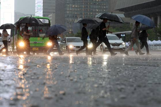 People walk through a waterlogged street at Gwanghwamun Square in central Seoul as heavy rain falls across the country on the morning of July 17. [NEWS1]